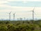 Wind turbines with clouds in the background and trees in the foreground.