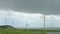 Wind turbines spinning in green field under gray stormy sky, bad rainy weather