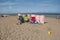 Windbreak with red and white stripes with three camping chairs and other beach objects.