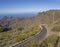 Winding asfalt road to village Masca with green hills, sharp mountain peaks, sea horizon clear blue sky background