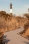 Winding boardwalk pathway leading to a large lighthouse. Fire Island New York