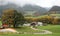 A winding country road curves between green fields and autumn trees leading to a farmhouse on a beautiful hillside