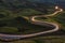 Winding curvy rural road with light trail from headlights leading through British countryside.