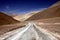 Winding dirt road leading into arid valley with barren dry yellow and brown hills in Atacama desert, Chile