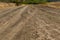 A winding wide road with turns of dust, earth and sand, among dry vegetation and grass. On the background of a beautiful cloudy sk