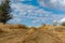 A winding wide road with turns of dust, earth and sand, among dry vegetation and grass. On the background of a beautiful cloudy sk