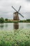 Windmill and bushes on the bank of a large canal in a cloudy day at Kinderdijk.