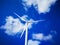 Windmill close up on blue sky and white cloud background. Wind-turbine on wind farm in rotation to generate electricity energy on