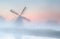 Windmill in dense fog at summer sunrise