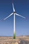 Windmill for electric power production. Wind power generator. Three-bladed wind turbine in desert field under intense blue sky.