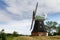 Windmill individually in the landscape against a blue sky from the side with brick base and covered with shingles and green roof