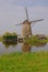 A windmill next to a house in kinderdijk with beautiful weather & water reflection