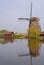 A windmill next to a house and tree in kinderdijk with beautiful water reflection