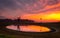 Windmill by pond in rural field with vivid sunrise