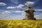 windmill stands in a field of vibrant yellow flowers under a sky filled with fluffy white clouds, ai generative
