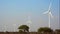 Windmill turbines producing environmental friendly green, clean electricity with trees at the bottom and blue sky and clouds in th