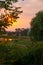 A windmill beside a willow tree during a stunning sunset