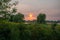 A windmill beside a willow tree during a stunning sunset