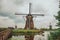 Windmills and bushes on the bank of a large canal in a cloudy day at Kinderdijk.