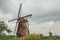 Windmills and bushes on the bank of a large canal in a cloudy day at Kinderdijk.