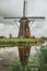 Windmills and bushes on the bank of a large canal in a cloudy day at Kinderdijk.