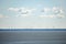 Windmills on the horizon with clouds in clear sky and sea in the foreground. Wind turbines, wind farms making electric power,