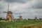 Windmills and tall bushes on the bank of a canal in a cloudy day at Kinderdijk.