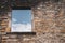 Window in ancient stone wall of damaged house, toned. Abandoned medieval building, filtered. Blue sky in window of ruin temple.