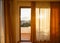 Window of a balcony with transparent curtains and view of morning sun and small resort town in mountains