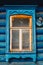 Window of blue cottage in russian traditional style with beautiful carved wooden frame and yellow sealing foam