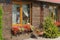 Window and brown wooden wall of the house and flowerpots with decorative plants and flowers in the street