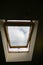 Window in the ceiling. Blue sky with clouds. Attic interior