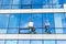 Window cleaner two person back to camera dangerous work at height outside of building glass exterior blue and white wall