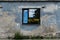 Window in an eroded plaster wall. Window with security grid and flower pot