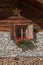 Window with geranium flowers, alpine hut with stone and wood facade, storage of logs