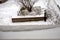 Window sill with an irregular layer of frozen snow on it. In the background is view on the yard covered with snow.