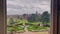 Window view of a grand garden with a fountain in the centre and neatly arranged bushes and trees