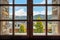 Window with a view to the ridge of mountains, snow-capped peak, clouds, sky, trees and houses in Andorra