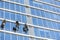 Window washers wash skyscraper windows sitting on hanging seats