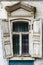 A window with wooden shutters and carved frames of the old house, with stucco elements on the facade