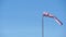 Windsock with red and white stripes show direction of wind blowing and speed. Cone wind indicator develops on blue sky background