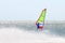 Windsurfer on a board with a sail on a water surface shrouded in spray