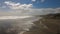 Windy Day on the Wide Brown Sand Beach at Low Tide. Cloudy Sky With the Sun Shining. Small Silhouettes of a Few Walkers