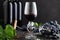 Wine glass with cold red wine. Wine bottles, grape bunches with leaves and vines on dark rustic concrete background. Wine