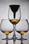 Wine glass goblets on short legs. Nearby is a glass on a long leg, a funnel is inserted into it. They have a small amount of