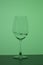 Wine glass on a long stem. A little drink is poured into it, a splash is visible. In back green