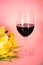 Wine glass with tulips on table, pink background