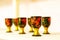 Wine glasses decorated with ornaments in the style of Russian Khokhloma standing on a wooden shelf.