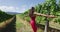 Wine tour in wine country. Woman in pink dress running amidst grapevines. Young cheerful female is enjoying at vineyard
