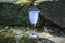 Wineglass with blue cocktail on rock, stones among moss. Scenic still life with alcoholic drink in nature. Blue lagoon from liquor